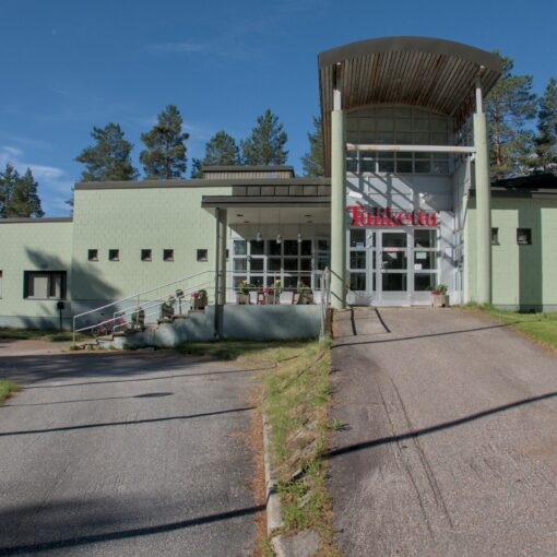 Hotellirakennuksen julkisivu. Keskellä katettu sisäänkäynti ja oven päällä nimi Tulikettu. Siitä vasemmalle laskeutuu portaikko ja yksikerroksinen rakennus laskeutuu kolmessa osassa kohti kuvan vasenta reunaa. Oikealla sisäänkäynnille johtava asfalttiluiska ja kuvaajaa kohti oikeassa reunassa suorakulmaisesti tuleva yksikerroksinen siipi. Rakennuksen takana on mäntyjä, etualalla asfalttipiha.